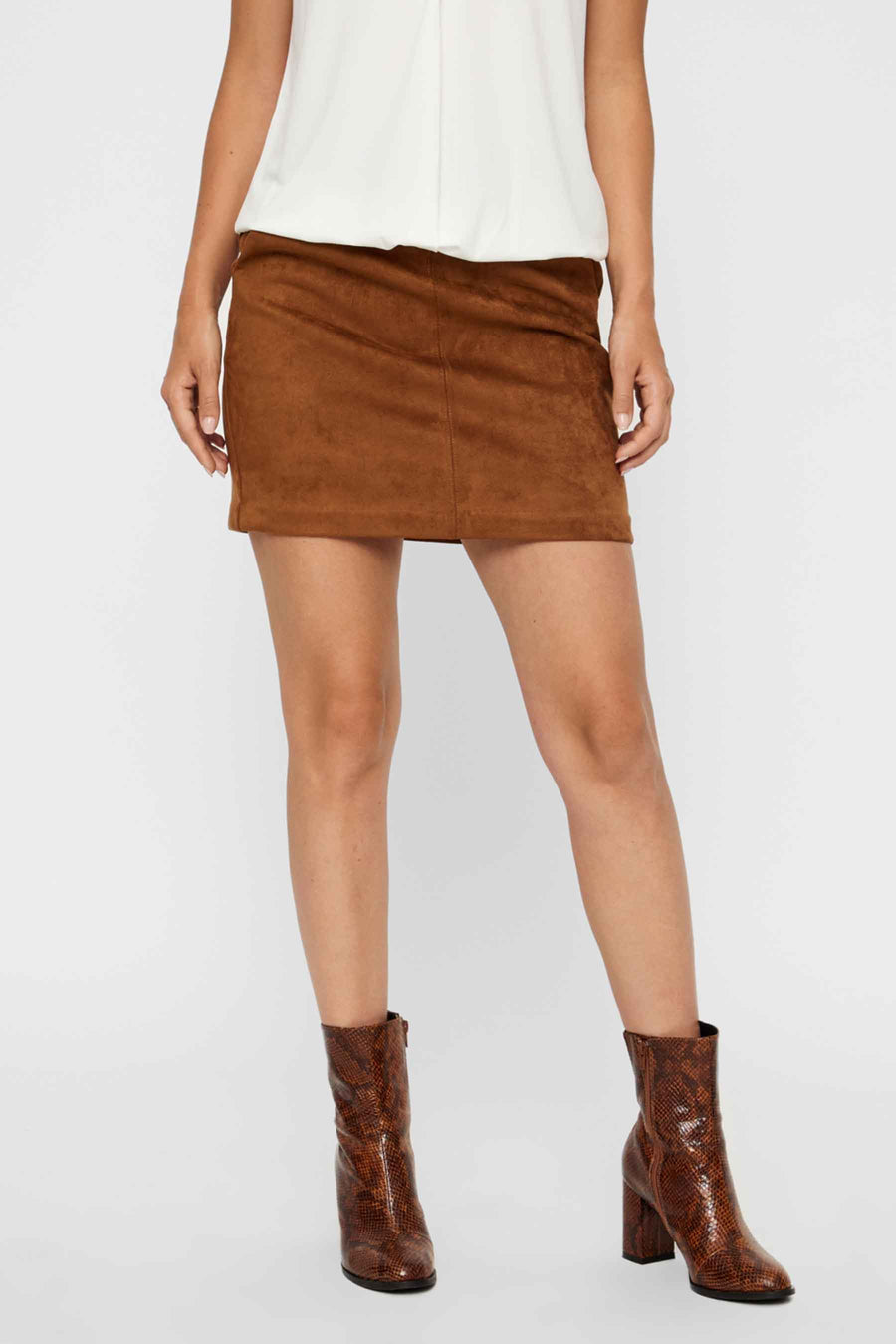 Mini-jupe marron en daim synthétique de Vero Moda, portée avec un haut blanc et des bottines à imprimé serpent.