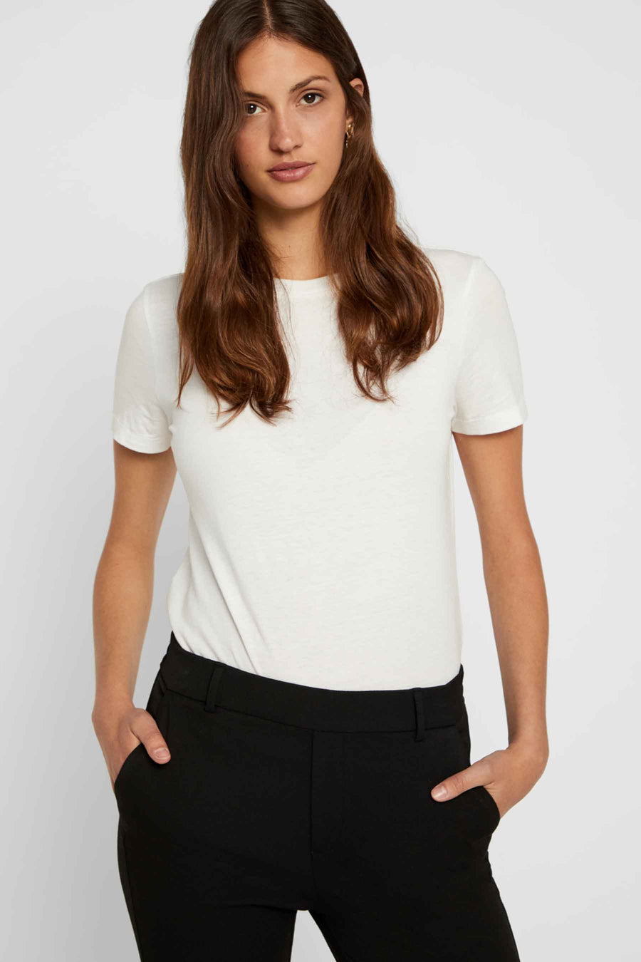 Pantalon costume noir de VERO MODA, porté avec un t-shirt blanc et les mains dans les poches.
