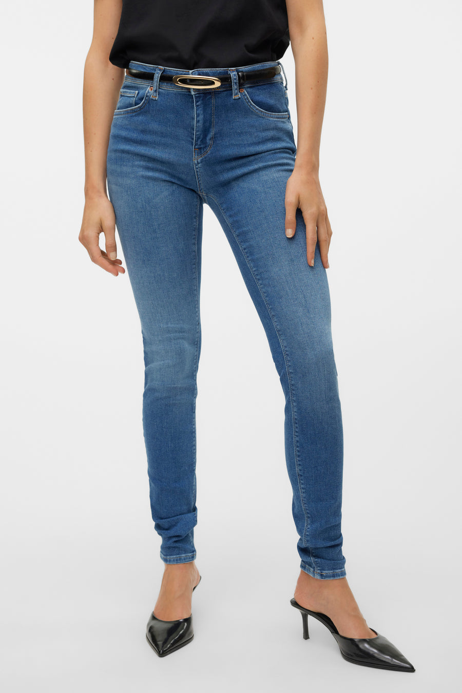 Jean skinny bleu moyen de VERO MODA, porté avec une ceinture noire à boucle dorée et des talons noirs pointus.
