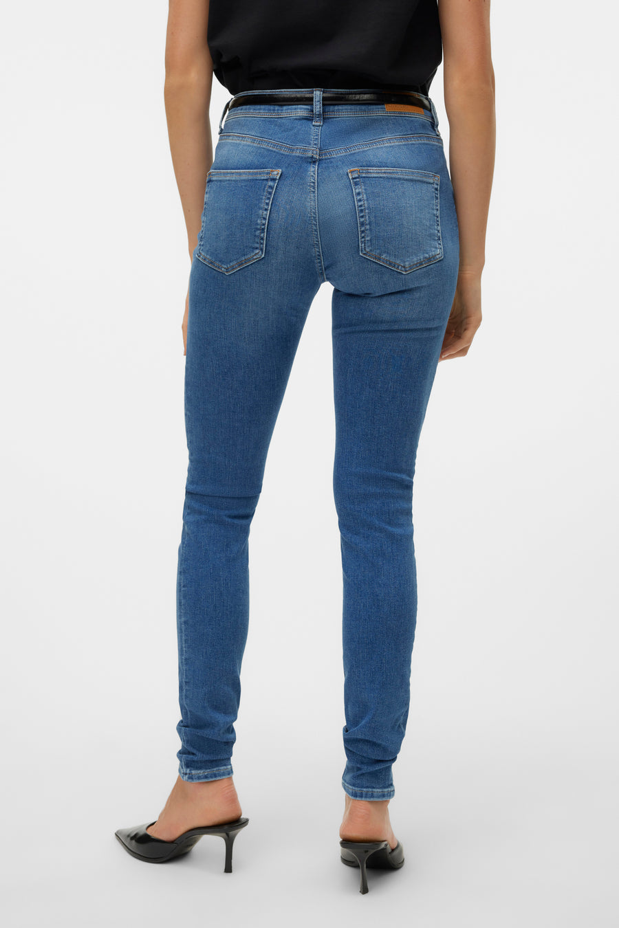 Jean skinny bleu moyen de VERO MODA, avec une ceinture noire et des escarpins noirs à talons aiguilles.
