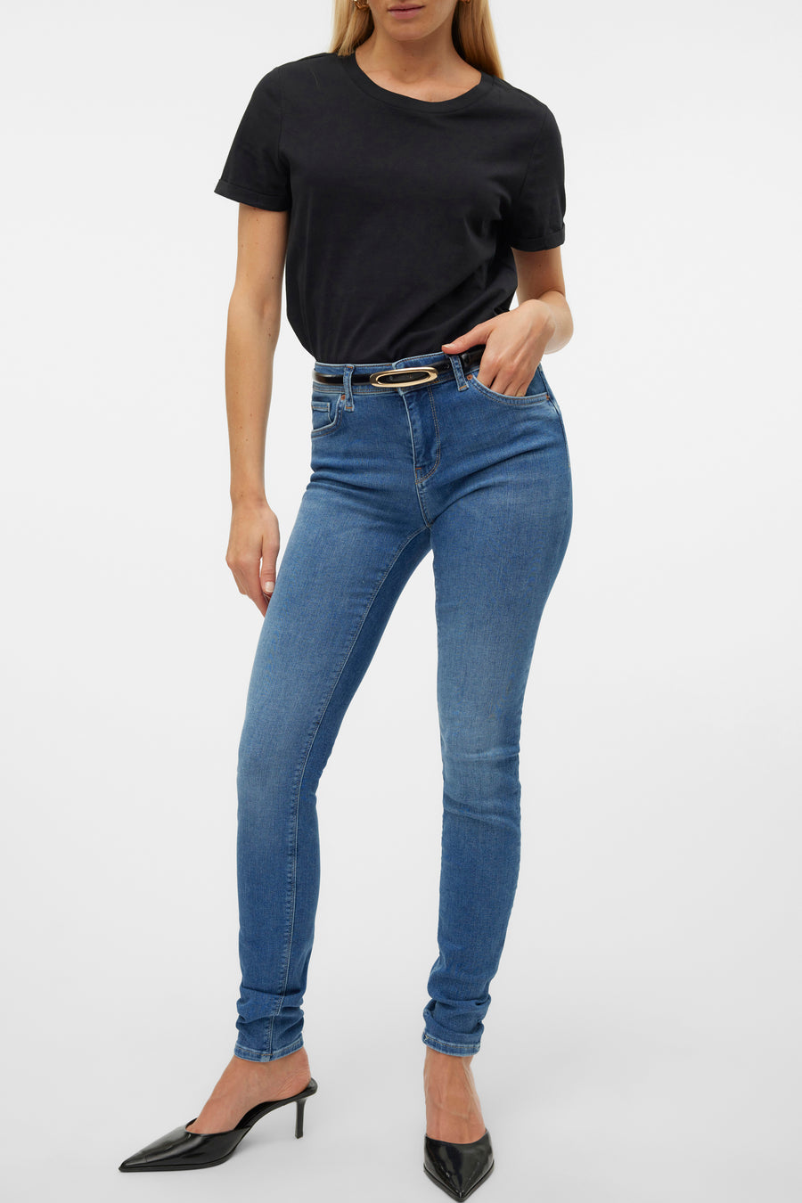Jean skinny en denim bleu moyen de Vero Moda, porté avec une ceinture noire et des escarpins noirs.
