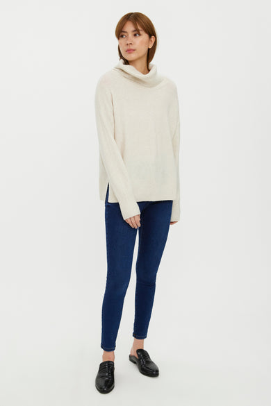 Pull col montant beige de VERO MODA, porté avec un jean bleu foncé et des mules en cuir noir.
