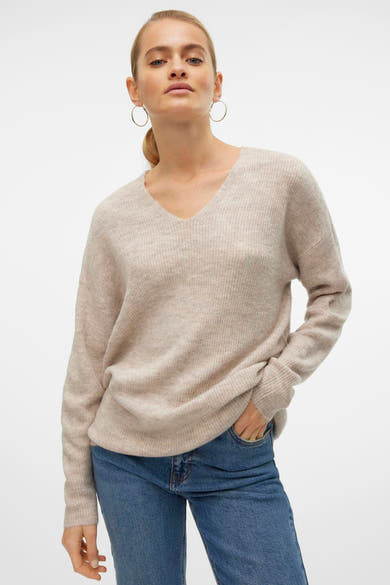 Ecru V-hals trui van VERO MODA, gedragen met een blauwe jeans, oorringen en een paardenstaart.