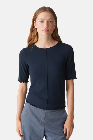 Pull à col rond bleu d'OPUS, avec détail de bordure festonnée et porté avec un pantalon gris.
