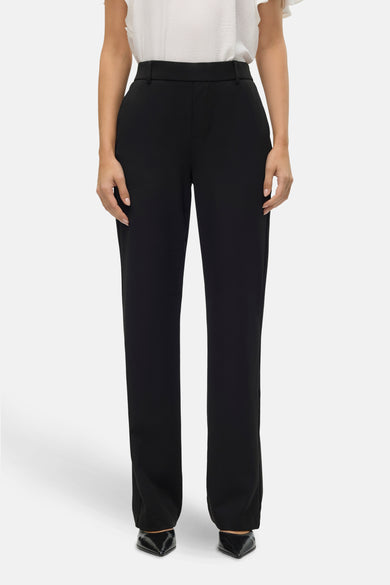 Pantalon noir de VERO MODA, coupe droite et poches discrètes, porté avec un haut blanc texturé et des escarpins noirs vernis.