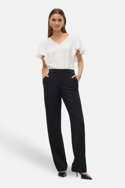 Pantalon noir de VERO MODA, coupe droite, porté avec un chemisier blanc à manches à volants et des escarpins pointus.
