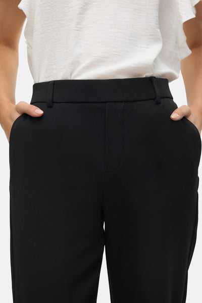 Zwarte broek van VERO MODA, gedragen met een witte bovenkleding, de handen in de zakken.