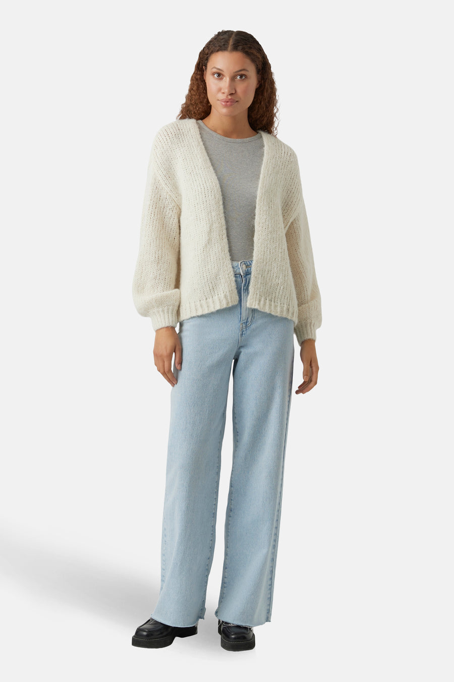 Beige vest van VERO MODA®, gedragen over een effen grijs T-shirt en een lichtblauwe wijde jeans.