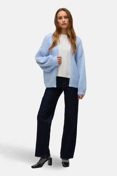 Cardigan bleu en maille de VERO MODA, porté sur un t-shirt blanc et un jean foncé avec des chaussures à talons.

