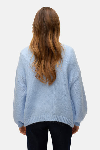 Cardigan bleu clair de VERO MODA, manches longues amples, texture douce et cheveux roux ondulés, vue de dos.
