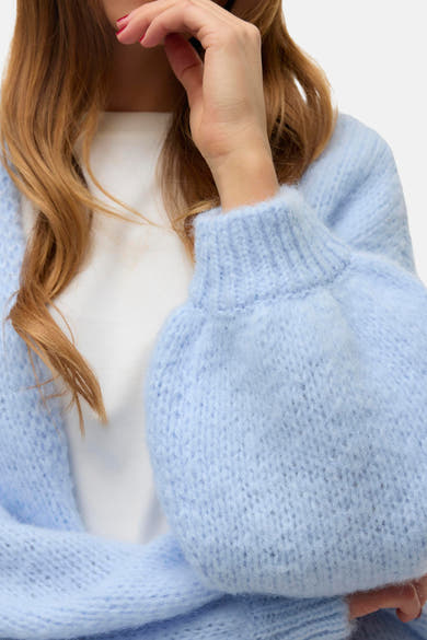 Cardigan bleu clair de VERO MODA, en tricot épais avec manches bouffantes, porté sur un t-shirt blanc.
