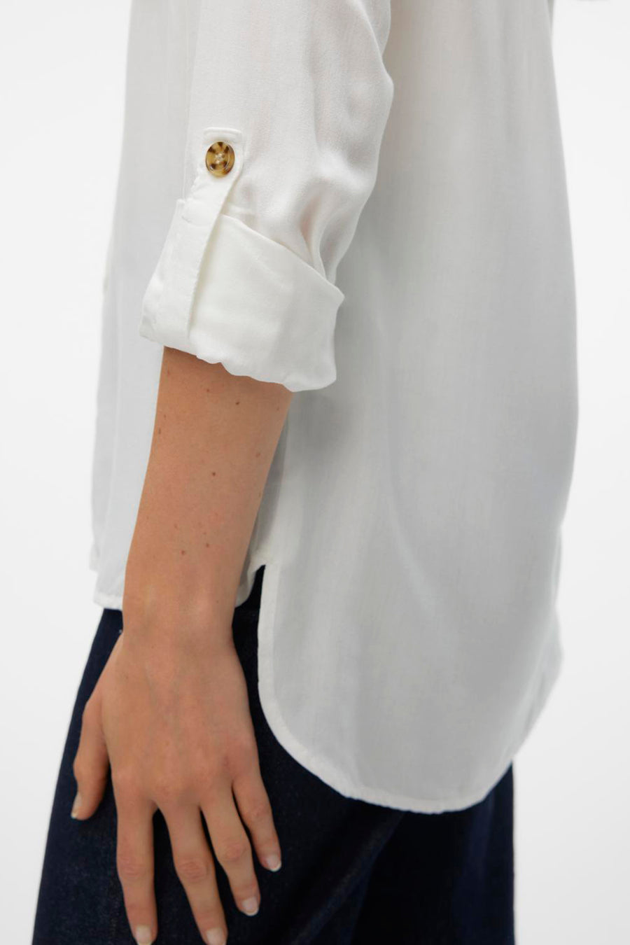 Chemisier blanc à manches longues de VERO MODA, avec manches retroussées boutonnées et ourlet arrondi, porté avec un pantalon bleu marine.