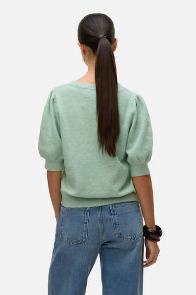 Groene trui met ronde hals van VERO MODA, met pofmouwen, gedragen met een blauwe jeans en bruine armbanden.