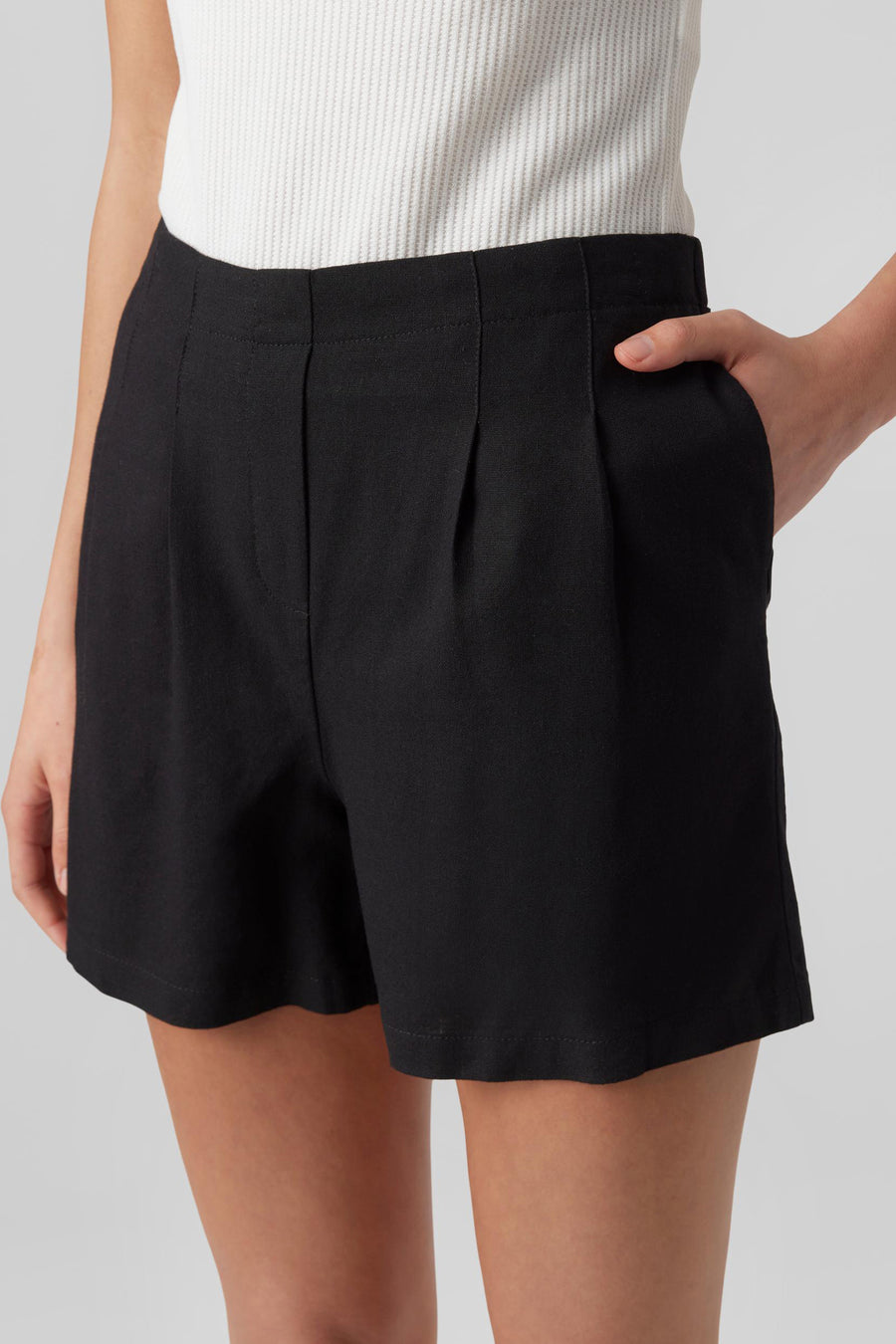 Short noir de Vero Moda, avec plis sur le devant et une personne avec une main dans une poche.