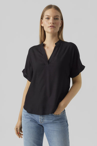 Zwarte blouse met korte mouwen van VERO MODA, gedragen met een blauwe jeans en beige sleehakken, achtergezicht.