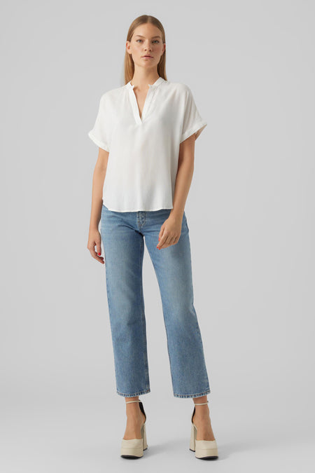 Blouse blanche à manches courtes de VERO MODA, portée avec un jean bleu et des chaussures à talons plateforme.