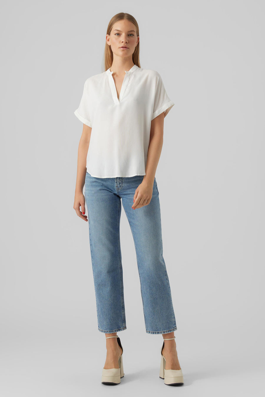 Blouse blanche à manches courtes de VERO MODA, portée avec un jean bleu et des chaussures à talons plateforme.