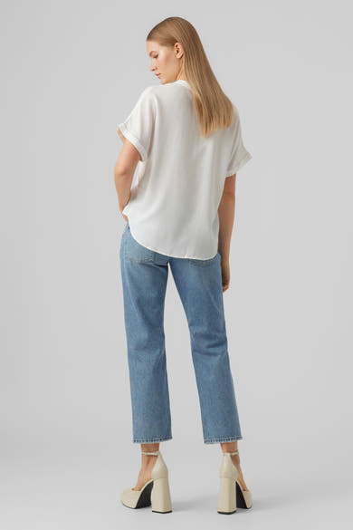 Chemisier blanc à manches courtes de VERO MODA, porté avec un jean bleu et des chaussures à talons plateforme ivoire.