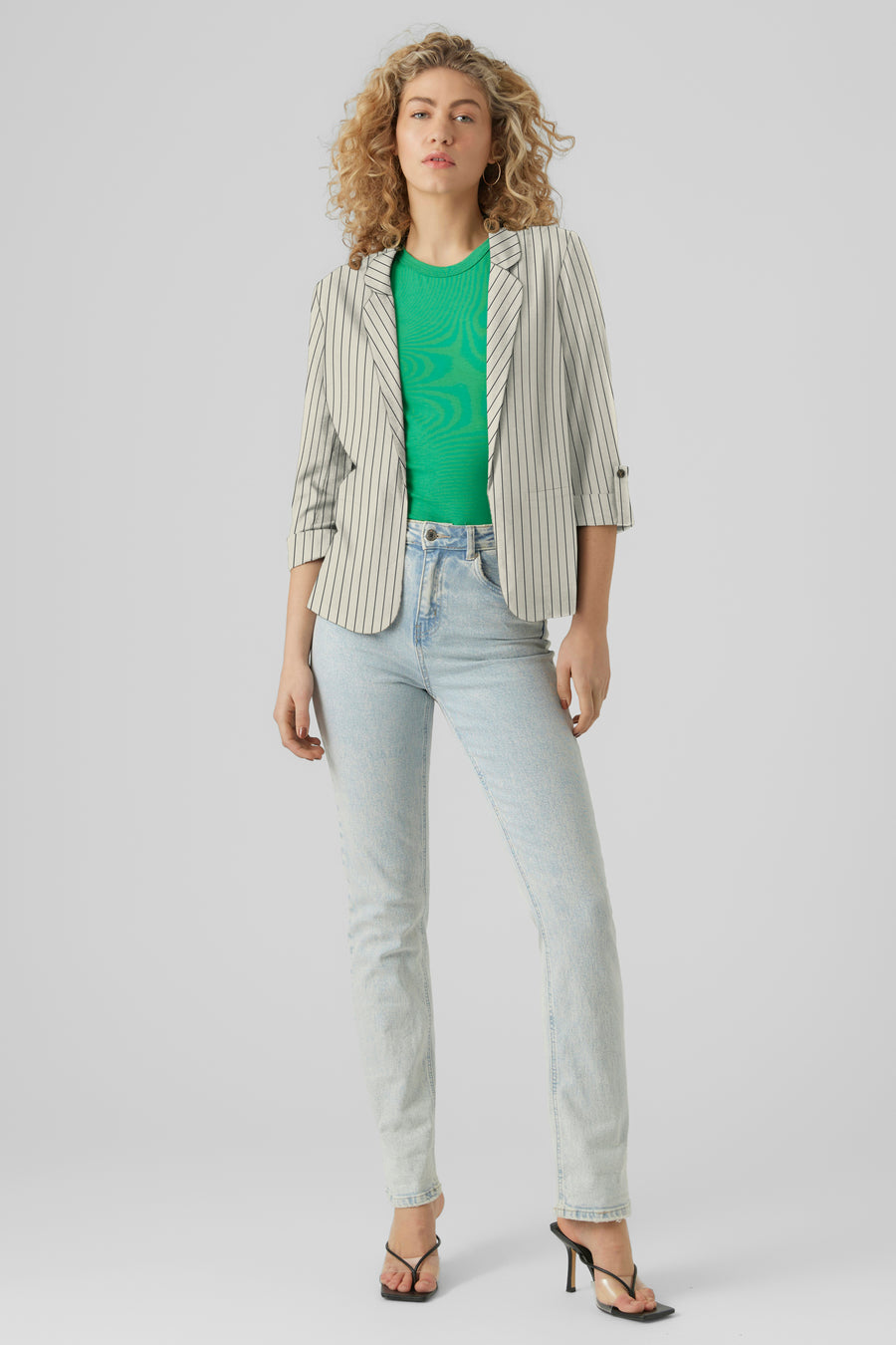 Blazer beige rayé par VERO MODA, porté sur un t-shirt vert et un jean délavé, avec des sandales noires à talons.
