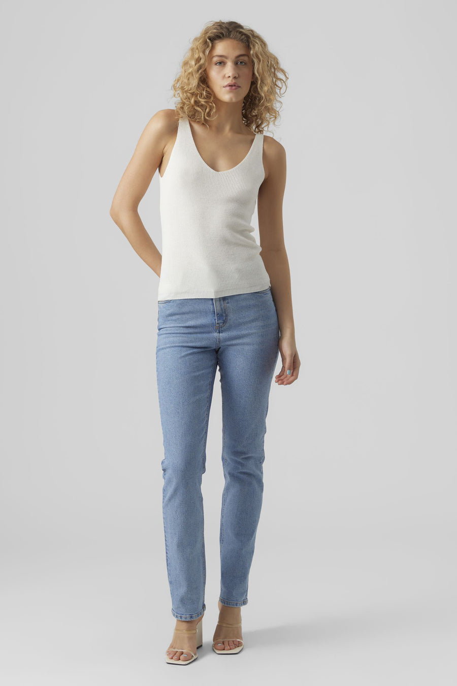 Top blanc à fines bretelles de Vero Moda, porté avec un jean bleu et des talons transparents.