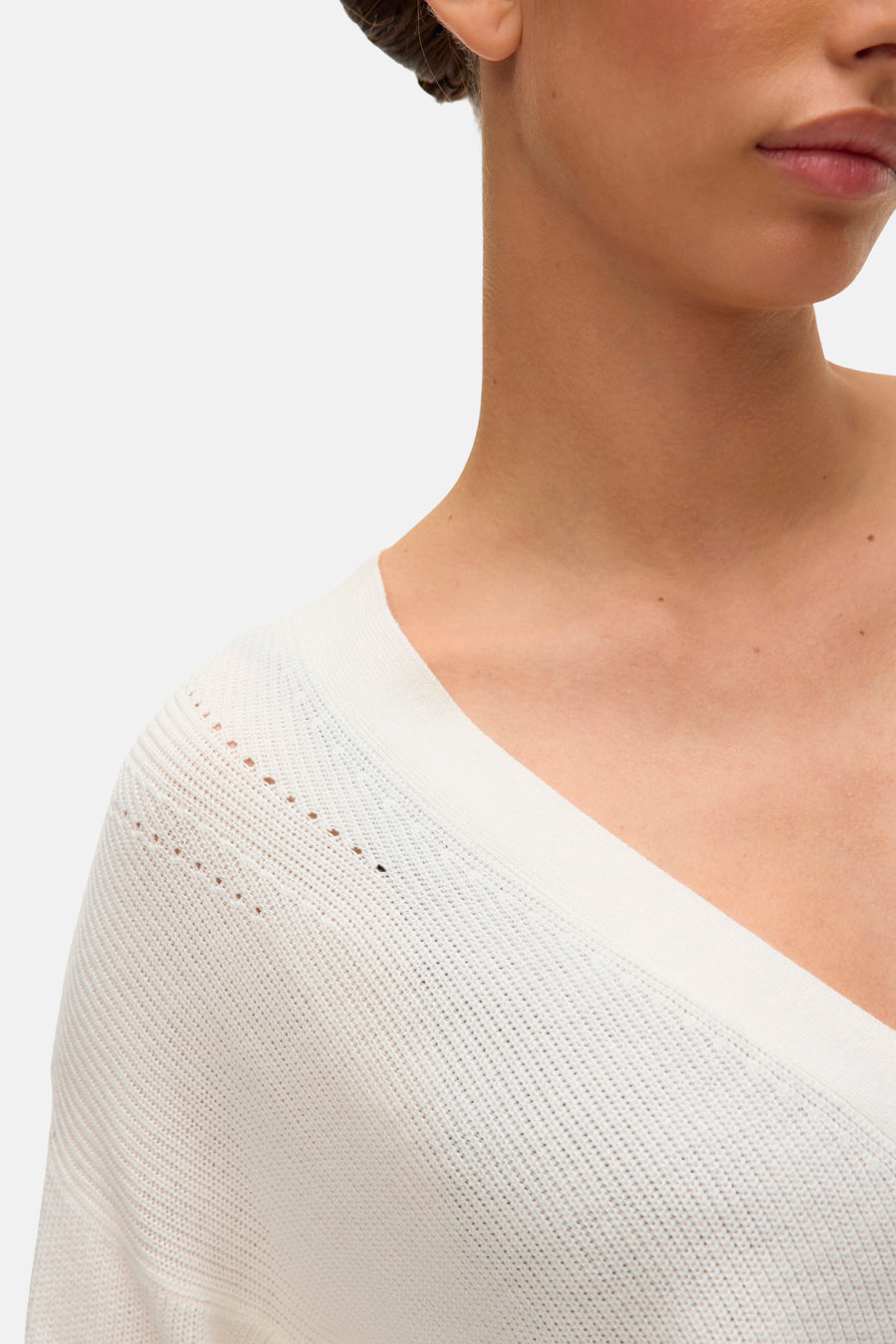 Gilet blanc de VERO MODA, en maille ajourée, col en V et coupe croisée, porté avec un chignon.
