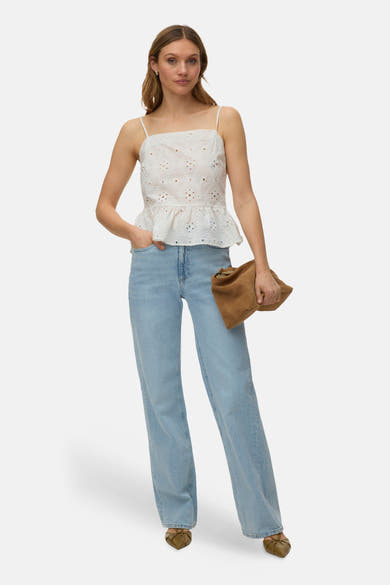 Jean droit bleu de VERO MODA, porté avec un haut blanc à broderies florales et des chaussures à talons.
