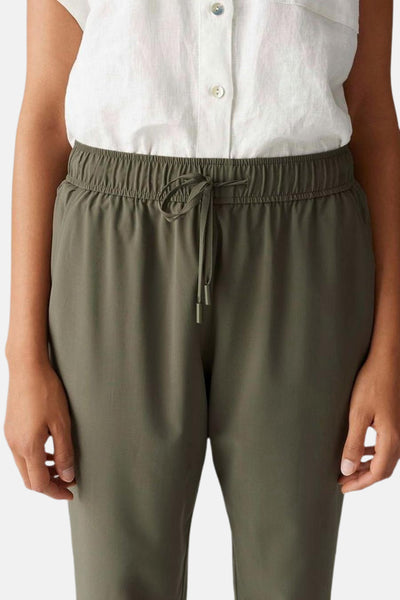 Pantalon coloré kaki de OPUS avec taille élastiquée à cordon de serrage, porté avec une chemise blanche.