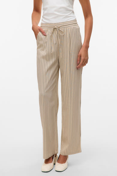 Pantalon beige à rayures verticales de VERO MODA, avec cordon de serrage à la taille, porté avec des ballerines blanches.
