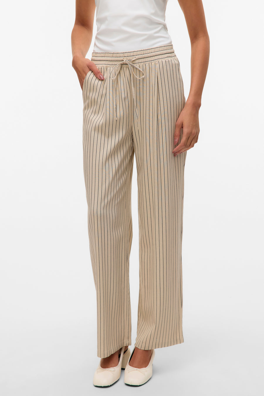 Pantalon beige à rayures verticales de VERO MODA, avec cordon de serrage à la taille, porté avec des ballerines blanches.
