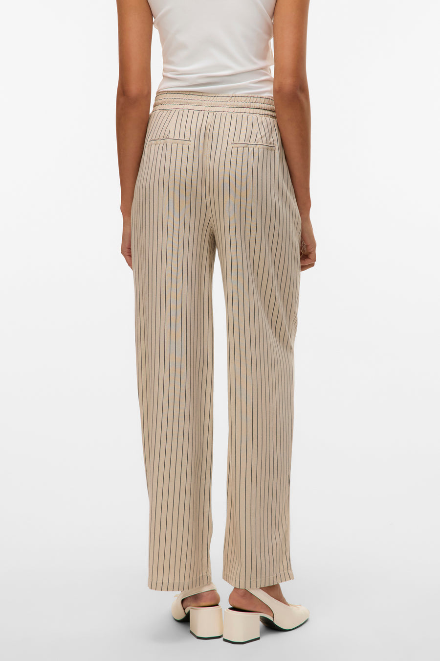 Pantalon beige rayé de VERO MODA, avec une taille élastique et des poches arrière, porté avec un haut blanc et des chaussures à talons clairs.