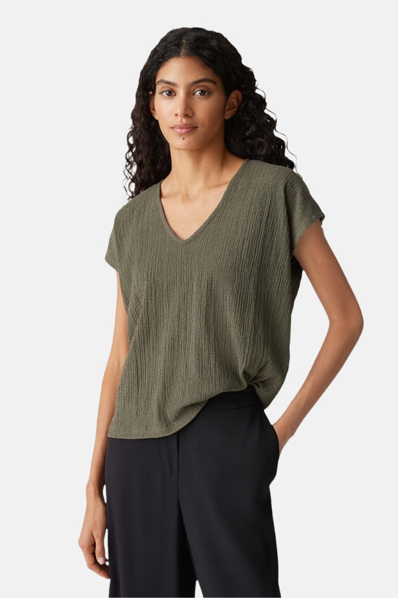 Blouse kaki à manches courtes par OPUS, avec une texture crêpe et un col en V, portée avec un pantalon noir.
