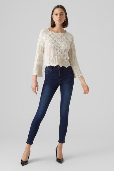 Pull beige en maille ajourée de VERO MODA®, avec manches trois-quarts et porté avec un jean bleu et des escarpins noirs.
