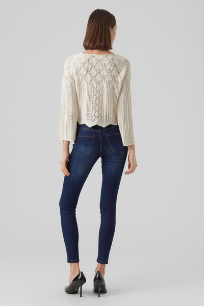 Pull beige ajouré de Vero Moda, porté avec un jean bleu foncé et des escarpins noirs.

