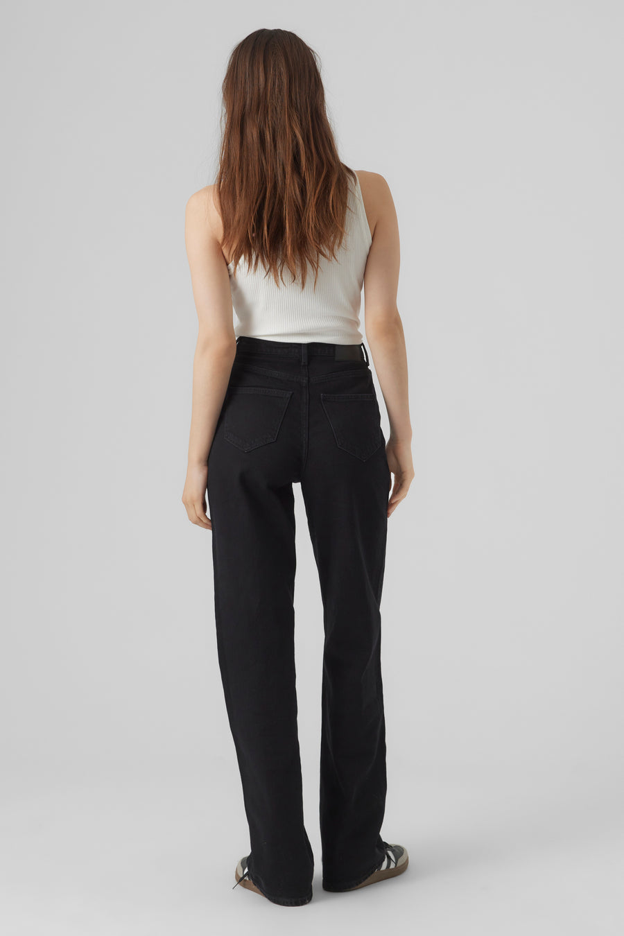 Rechte zwarte denim jeans van VERO MODA, gedragen met een witte geribbelde tanktop en sportschoenen.