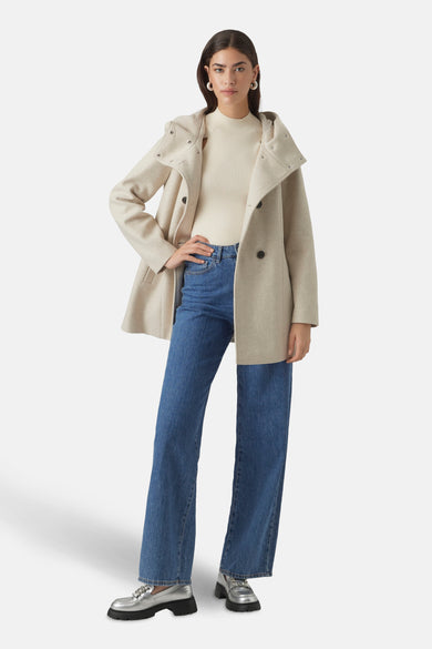 Korte beige jas van VERO MODA met capuchon en zwarte knopen, gedragen over een crèmekleurige trui en een wijde blauwe jeans.