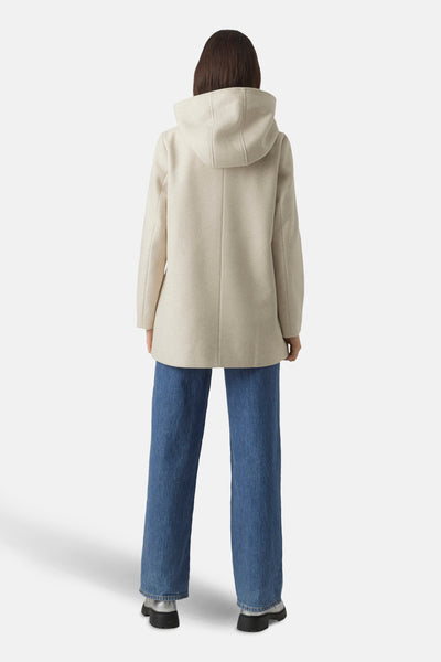 Korte beige jas van Vero Moda met capuchon, gedragen met een blauwe jeans en zilveren enkellaarsjes, van achteren gezien.
