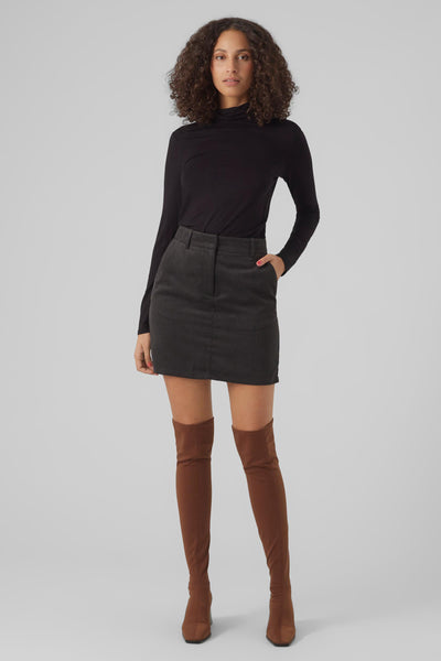 Haut à manches longues noir de Vero Moda, porté avec une jupe en velours côtelé et des bottes hautes marron.
