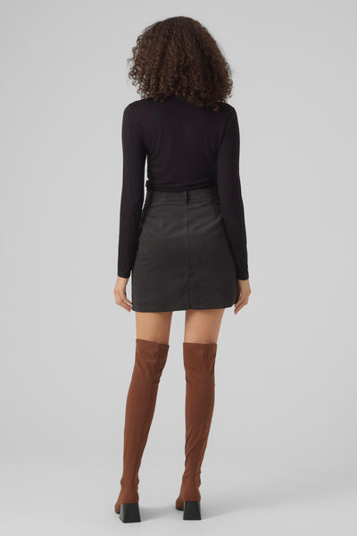 Zwarte top met lange mouwen van VERO MODA, gedragen met een gestreepte rok en hoge bruine laarzen.
