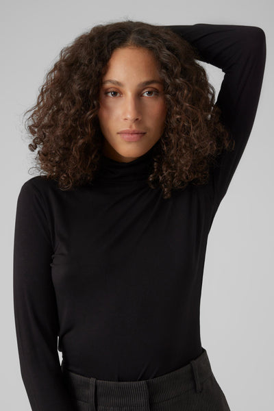 Top noir à manches longues de VERO MODA, porté avec un pantalon côtelé.