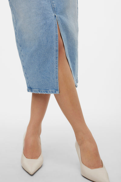 Jupe mi-longue en denim bleu clair de VERO MODA, avec fente sur le côté et portée avec des escarpins blancs.