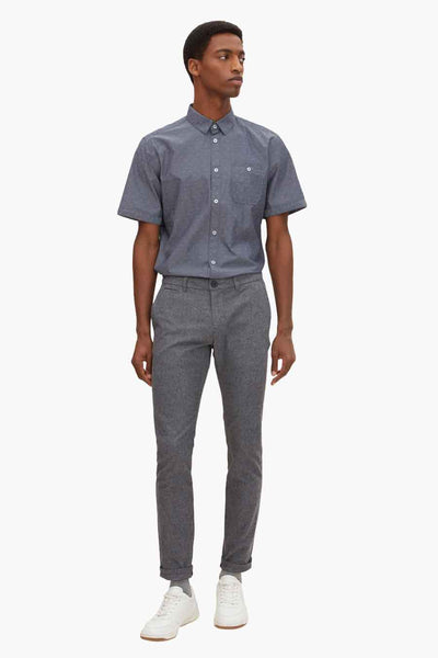 Blue short-sleeve shirt with subtle white dot pattern, button-down front and chest pocket, worn with gray trousers and white sneakers in full-length front view.