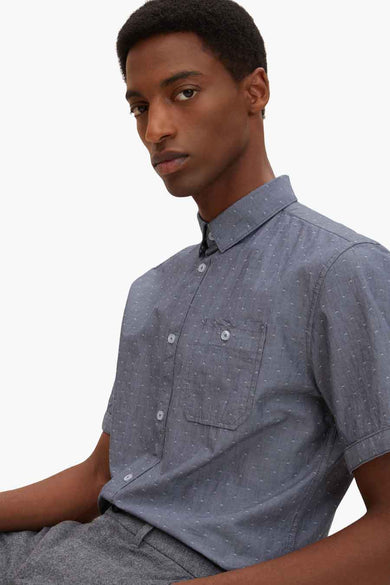 Blue short-sleeve shirt with white micro-pattern and chest pocket, side view on model wearing gray pants