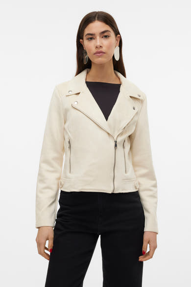 Veste en similicuir beige de Vero Moda, avec fermeture éclair asymétrique et porté sur un haut noir et un pantalon noir.