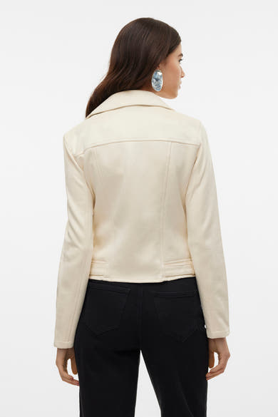 Veste en simili cuir beige de VERO MODA, vue de dos, portée avec un jean noir et des boucles d'oreilles.