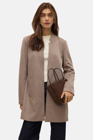 Lange jas van Vero Moda, gedragen over een witte trui met een handtas en een donkere broek.