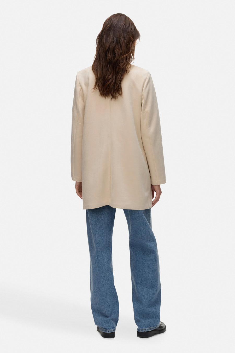 Ecru lange jas van VERO MODA, van achteren gezien, gedragen met een wijde blauwe jeans.