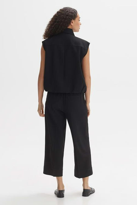 Zwart mouwloos vest van OPUS, van achteren gezien met een zwarte pantalon met een rechte pijp en zwarte platte schoenen.