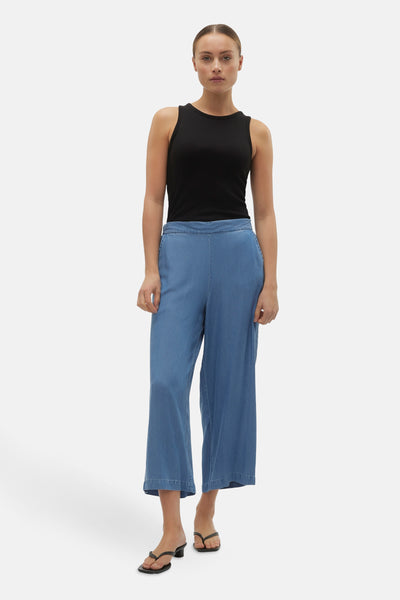 Pantalon denim bleu moyen de VERO MODA, jambes larges et courtes, porté avec un débardeur noir et des sandales.