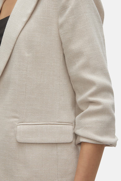 Blazer écru de VERO MODA, avec texture tissée visible et manches trois-quarts retroussées, en gros plan.
