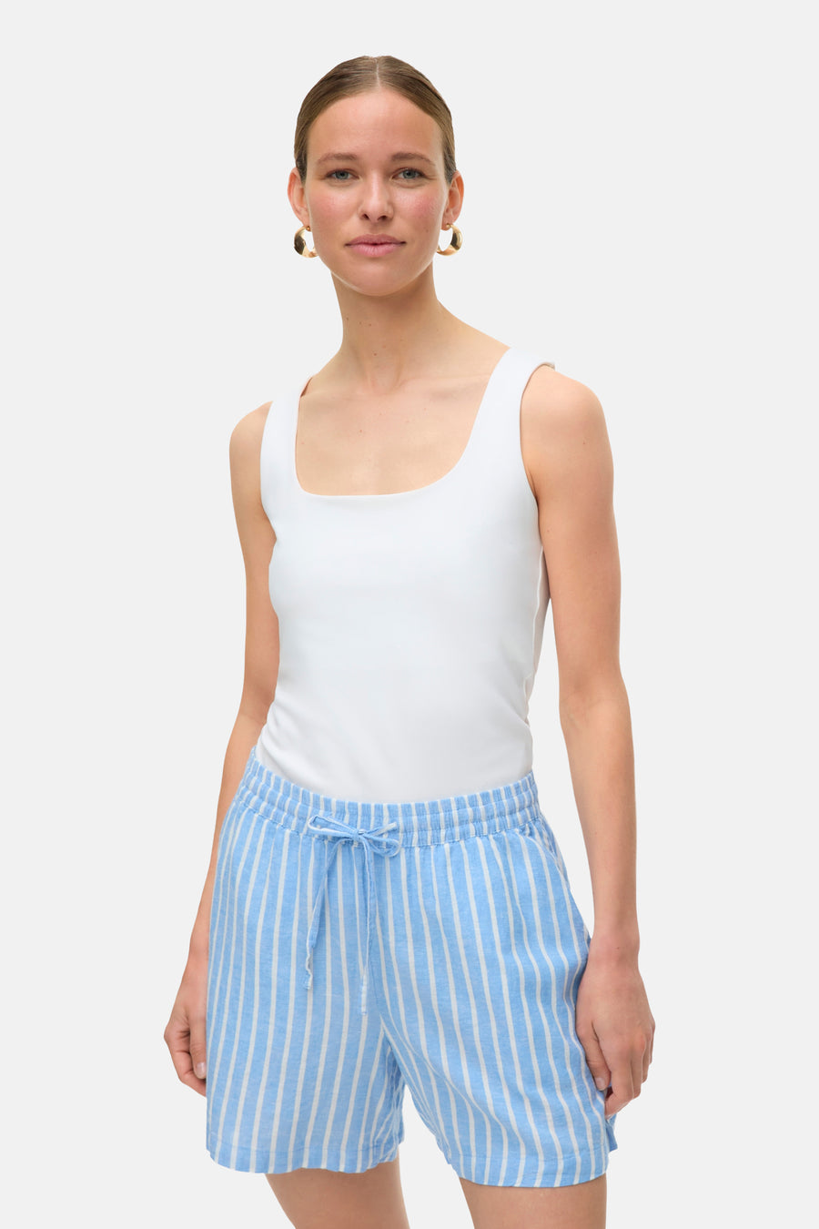 Short rayé bleu, de VERO MODA, avec cordon de serrage, porté avec un débardeur blanc et des boucles d'oreilles dorées.